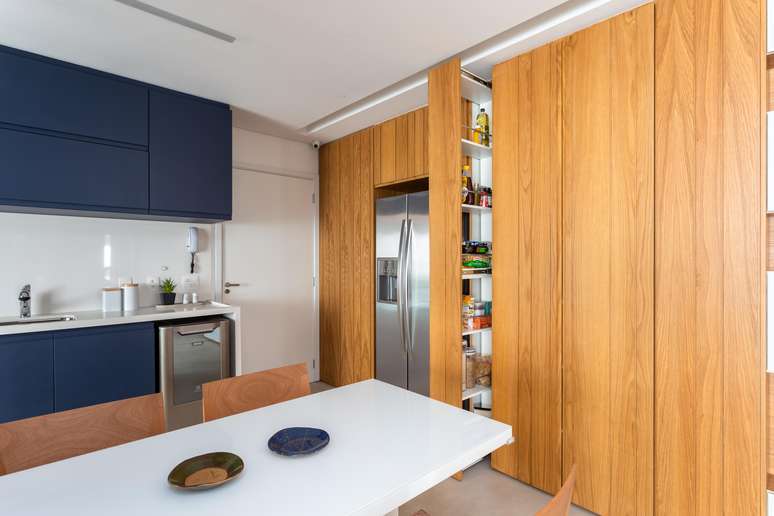 The main idea was to leave the pantry with easy and practical mechanisms for opening and closing its doors, one deeper and the other shallower, like that of a common wardrobe.  Another charm of the piece is the absence of any apparent knobs or handles, leaving the asset with a discreet and elegant finish.  With this solution created by Studio Tan-gram, the apartment has gained more space and freed the wardrobes from overloading, providing an excellent and discreet division of the kitchen.