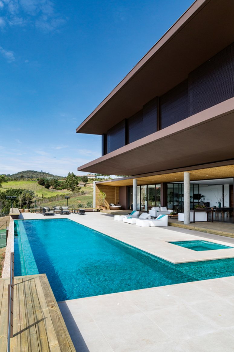 No piso da &aacute;rea externa desta casa de campo, o m&aacute;rmore travertino comp&otilde;e com as pastilhas da piscina. Projeto de Padovani Arquitetos+Associados.