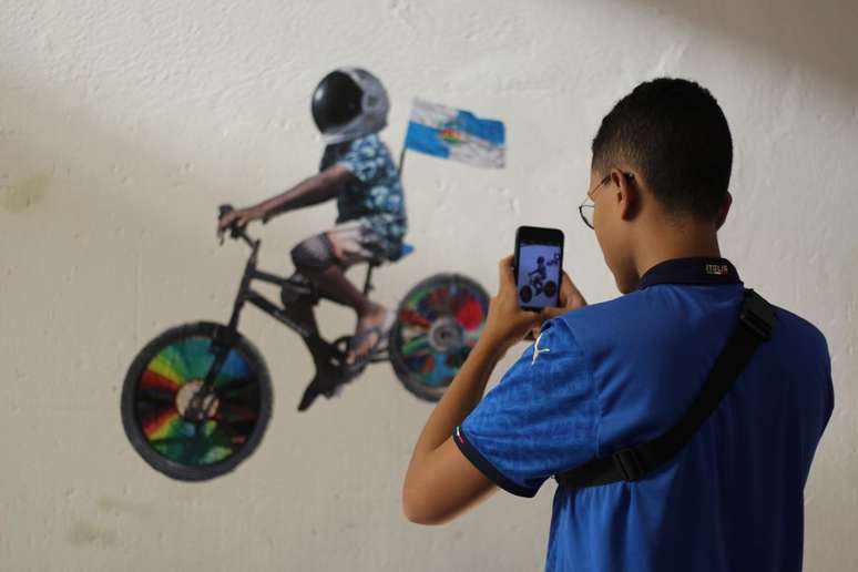 Na Exposição Bomba Relógio, com artistas da Baixada Fluminense, visitante fotografa obra “O menino na bike”