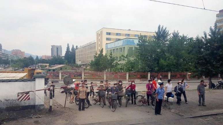 Foto tirada durante a pandemia mostra cidadãos esperando a passagem de um trem em um cruzamento em Pyongyang