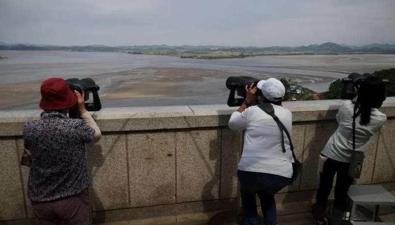Turistas na Coreia do Sul olhando para o norte atrav&eacute;s da Zona Desmilitarizada que separa os dois pa&iacute;ses