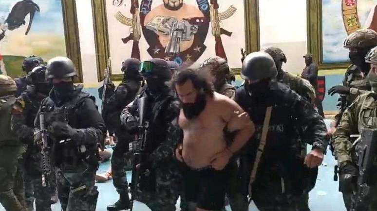 Jos&eacute; Adolfo Mac&iacute;as "Fito", barbudo, algemado e sem camisa, &eacute; levado pelas for&ccedil;as de seguran&ccedil;a para outra penitenci&aacute;ria