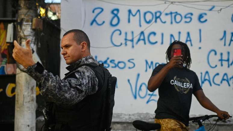 Foto mostra policial e um jovem negro atrás dele, em uma bicicleta, o filmando com um celular.