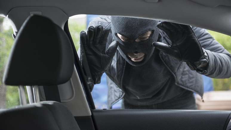 Ladrão encapuzado olhando através da janela de um carro