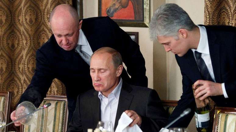 Yevgeny Prigozhin (esquerda) serve Vladimir Putin (centro) em um jantar em 2011