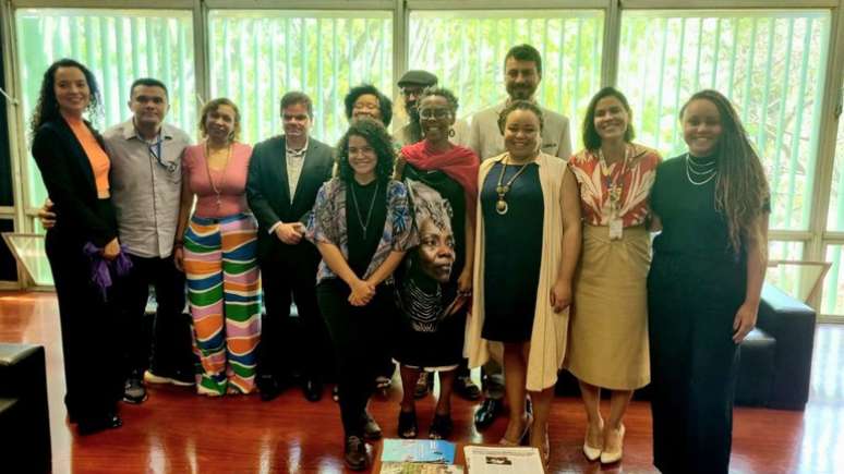 Doze pessoas de pé, em frente a uma ampla janela. São oito mulheres e quatro homens.