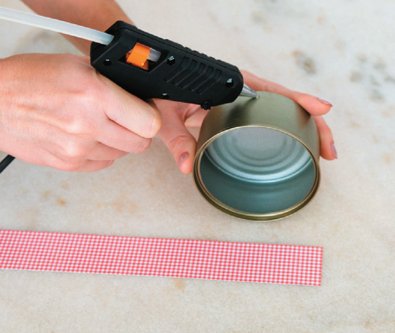 Manually applying hot glue to a can to make a tuna can lamp