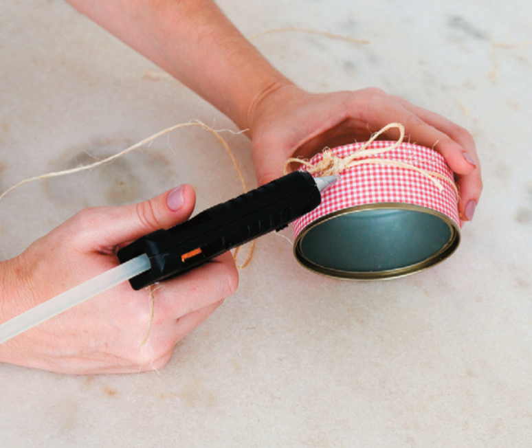 Manually applying hot glue to the string and can to make a tuna can lamp