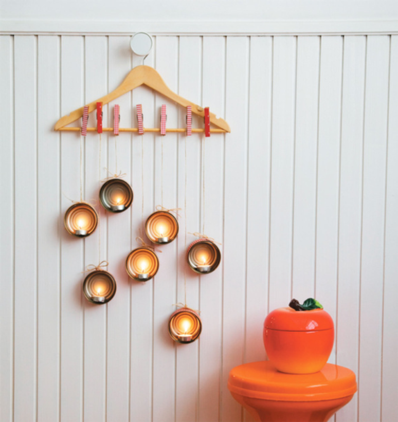 Lamp with tuna cans and finished candles hanging on a white wooden wall