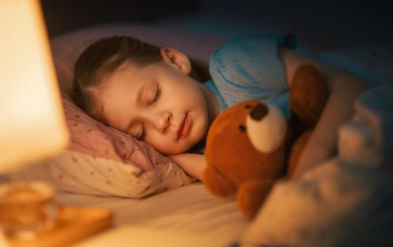 Criança dormindo com urso de pelúcia na cama