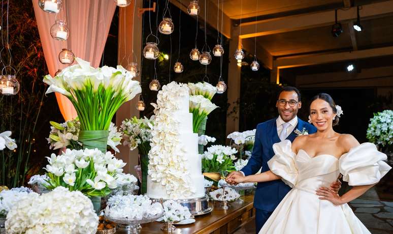 O casal ao lado da bela mesa de doces, com o bolo em destaque