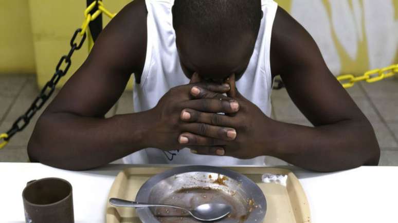 Imagem mostra uma pessoa negra de cabeça baixa diante de um prato vazio.
