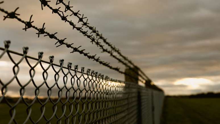 Imagem mostra arame farpado em cerca de presídio.