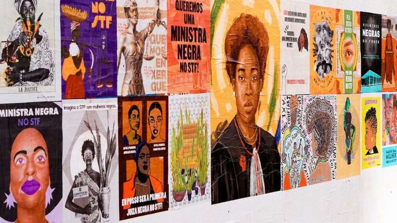 A imagem mostra uma parede branca com diversas artes de mulheres negras, parte da campanha da mulher negra para o STF. As artes, diferentes uma das outras, estão coladas lado a lado.