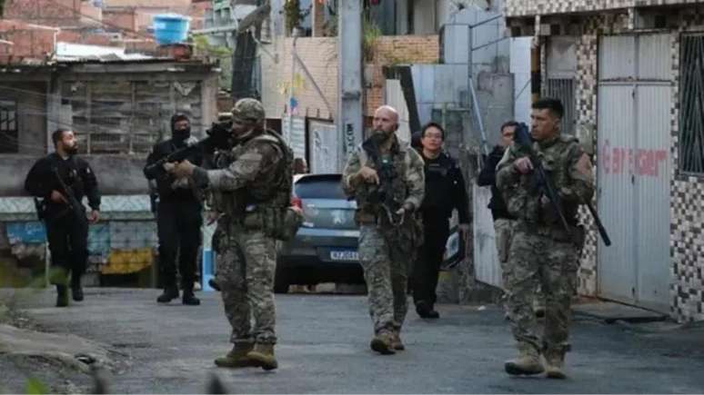 Imagem mostra alguns agentes militares armados caminhando por uma comunidade periférica durante operação.