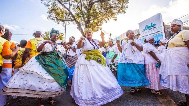 A imagem mostra um grupo de mulheres com trajes típicos da Bahia em celebração na via pública.