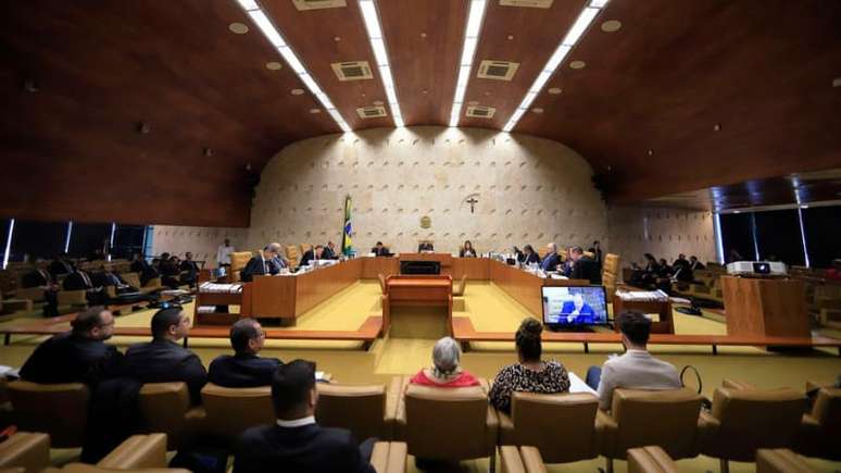 Imagem mostra uma sessão no Supremo Tribunal Federal, uma grande sala com os ministros sentados no centro e outros espectadores em sua volta.
