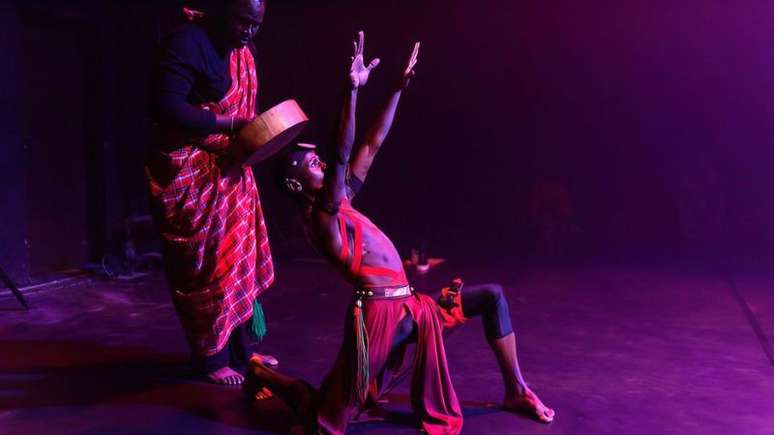 Imagem foca em dois homens negros em trajes vermelhos performando no palco.