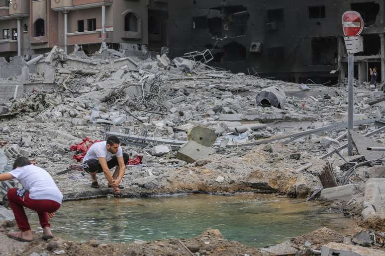 Palestino lava as mãos em uma poça ao lado de um prédio destruído após os ataques israelenses na Cidade de Gaza