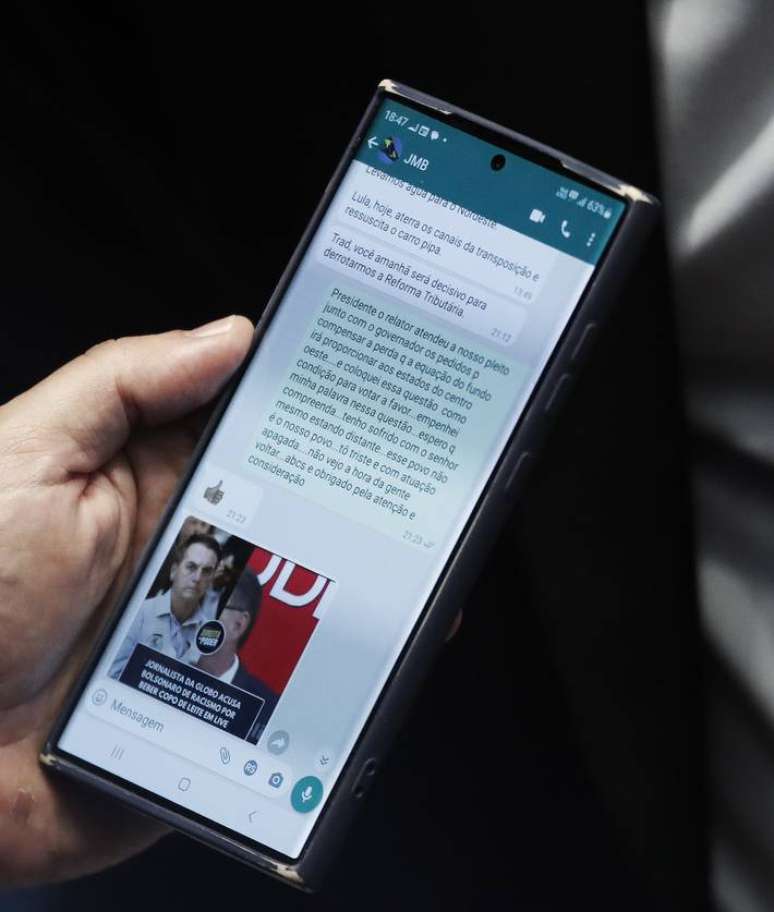 Celular nas mãos de Nelsinho Trad mostram o contato JMB, acrônimo de Jair Messias Bolsonaro, dizendo que o voto do senador era 'decisivo' para derrotar a reforma tributária; congressista nega e afirma que mensagem era do filho do ex-presidente, Flávio.