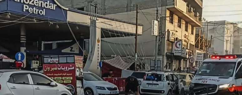 Um homem se abaixa para cuidar de uma pessoa ferida no chão depois que uma ambulância foi danificada em um suposto ataque israelense em frente a Al-Shifa, no dia 3 de novembro (a imagem foi cortada propositadamente para evitar mostrar conteúdo sensível)