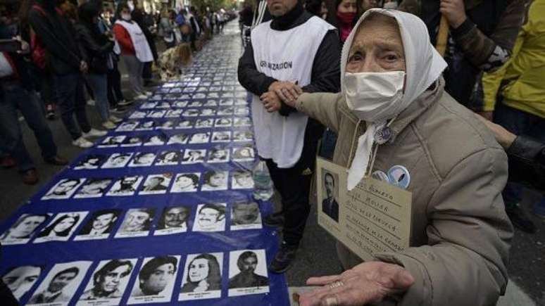 Adelina Lara Molina, integrante das Mães da Praça de Maio, ao lado de uma grande faixa com retratos de pessoas desaparecidas durante a ditadura militar argentina (1976-1983)