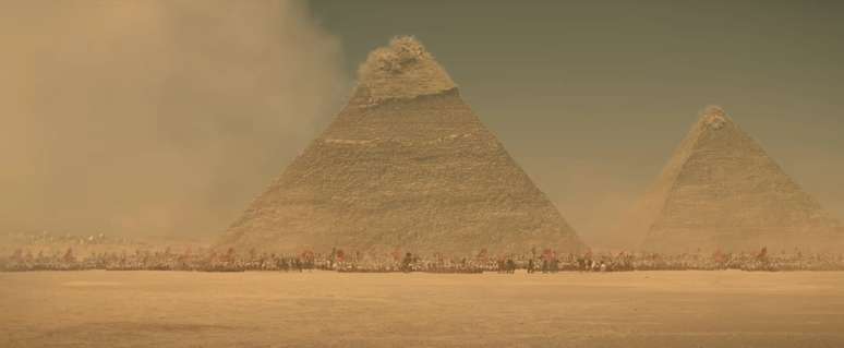 The top of one of the great pyramids explodes under cannon fire with an army ranged before it in Ridley Scott’s Napoleon
