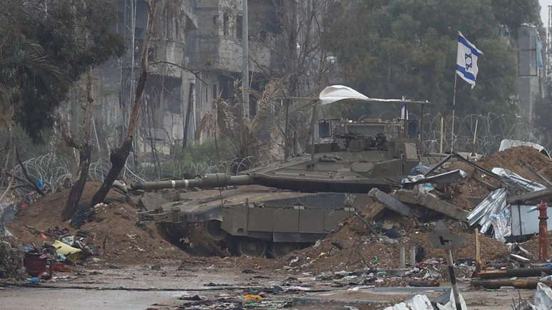 Uma bandeira israelense tremula no topo de um tanque, enquanto os palestinos que fogem do norte de Gaza vão para o sul durante uma trégua temporária entre Israel e o Hamas