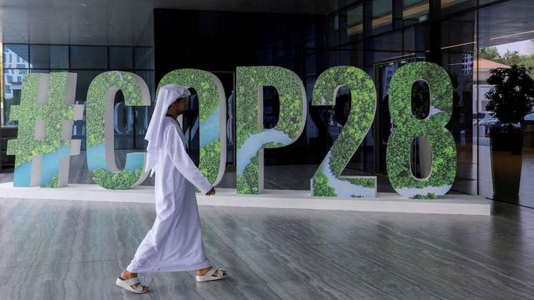 Homem passa na frente de letreiro com os dizeres COP28