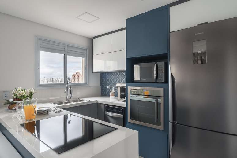 Projetada pela dupla de arquitetos do escrit&oacute;rio PB Arquitetura, a cozinha em modelo peninsular facilita a vida dos moradores no intuito de alcan&ccedil;ar utens&iacute;lios com mais facilidade. Entre os destaques, a bancada de pedra sint&eacute;tica branca.