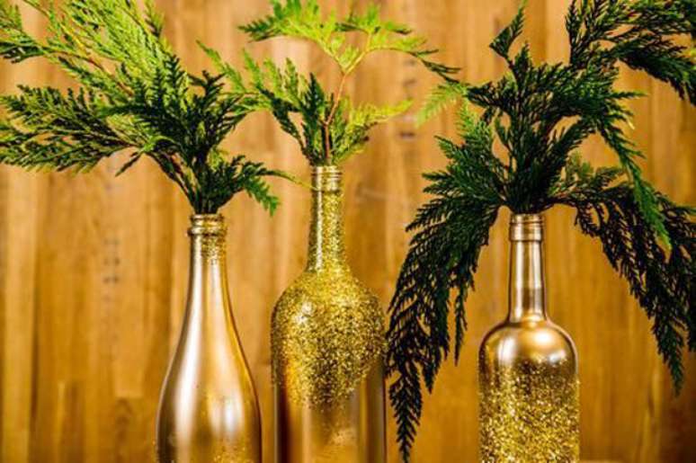 A decoração de Natal dourada está com tudo! Pinte suas garrafas com tinta e glitter e adicione ramos. Essa decoração funciona também para o ano novo.
