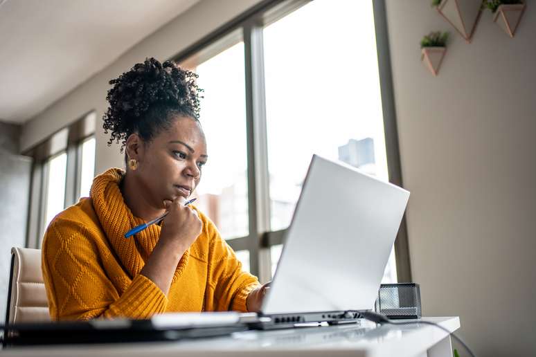 Mulher em frente a tela de um computador lendo o edital e um concurso. 