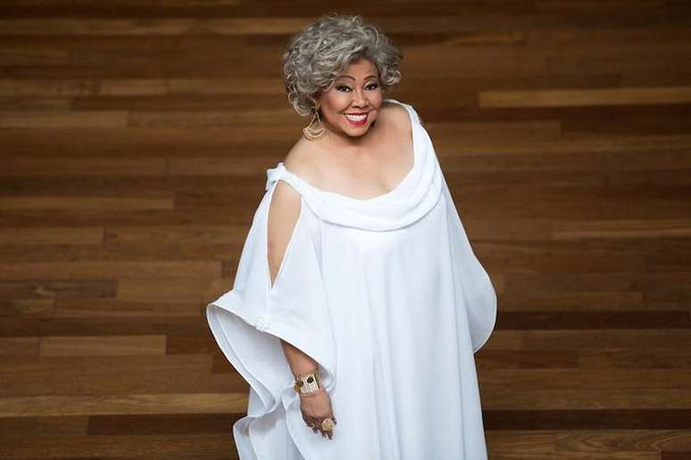 Imagem mostra a cantora Alcione de pé e com um vestido branco.