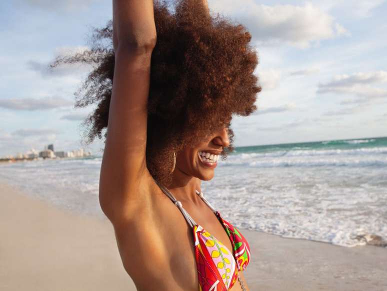 Imagem mostra mulher negra de cabelos crespos na praia.