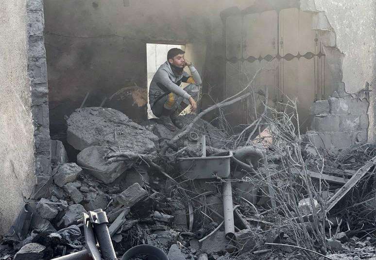 Homem agachado sobre escombros em Gaza