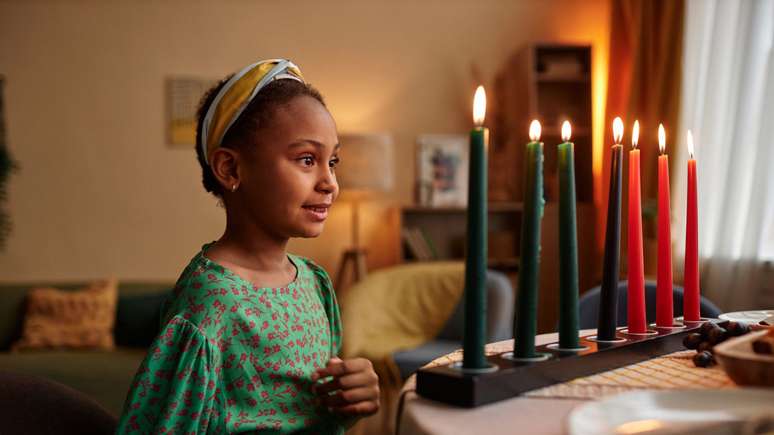 Imagem mostra uma menina negra ao lado de velas pretas e vermelhas, em celebração ao Kwanzaa.