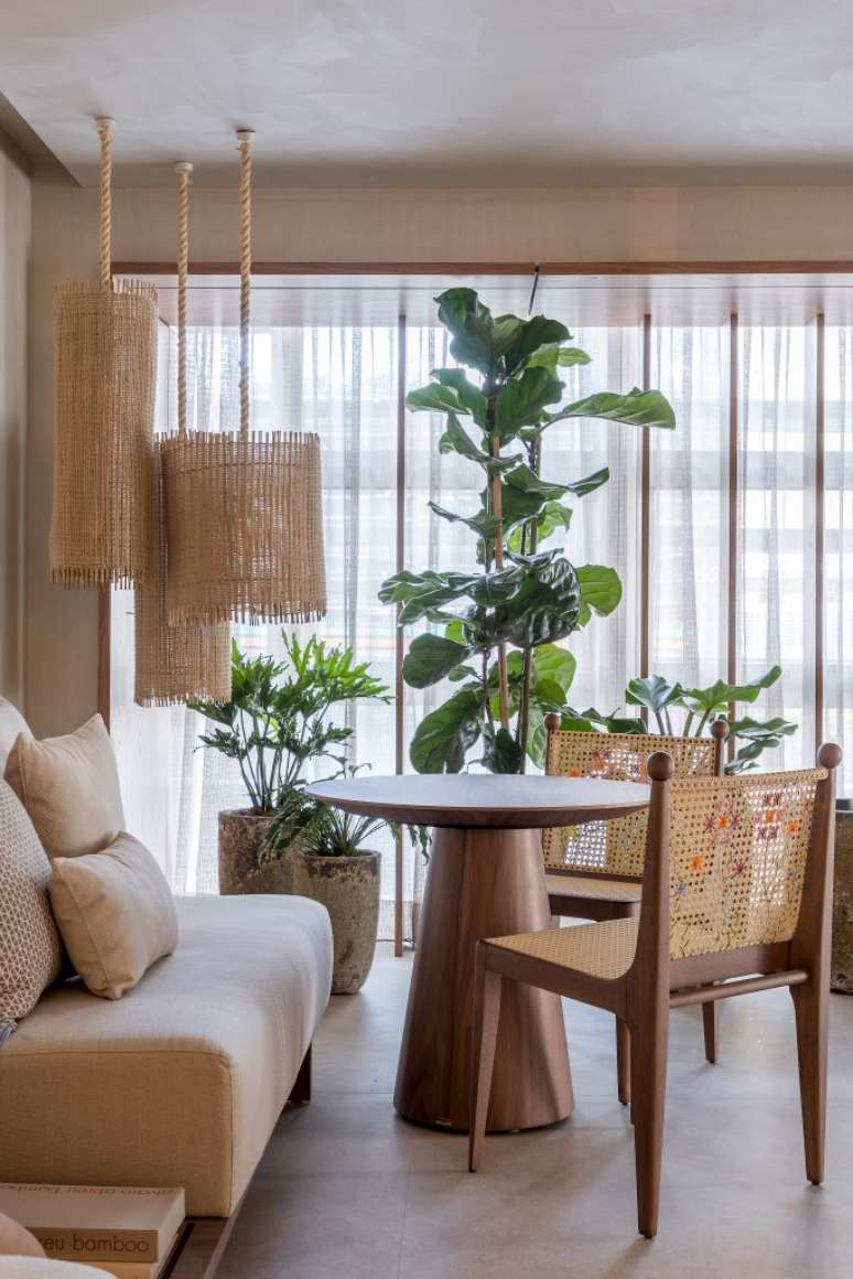 Living room in beige tones, round wooden table, cane chairs, cane lamp and plants. Living room in beige tones, round wooden table, cane chairs, cane lamp and plants.