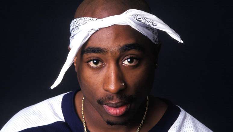 Imagem mostra Tupac, rapper negro, com o cabelo raspado e bandana dobrada na cabeça.