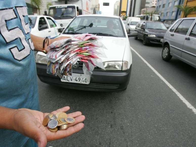 Imagem mostra um homem segurando balas e moedas que vende na rua.