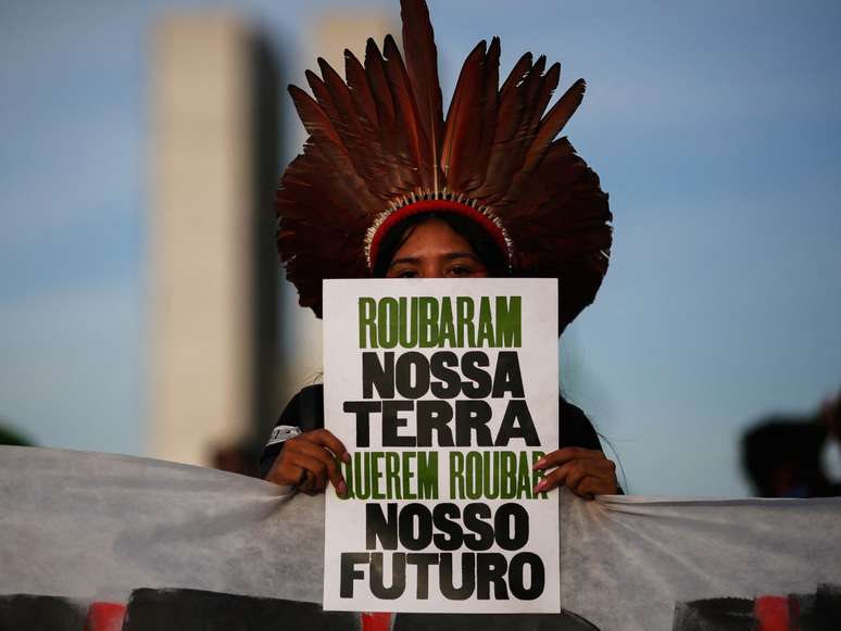 A imagem mostra uma mulher indígena segurando uma placa escrita "roubaram nossa terra, querem roubar nosso futuro",code freebet gratuitmanifestação contra o marco temporal.