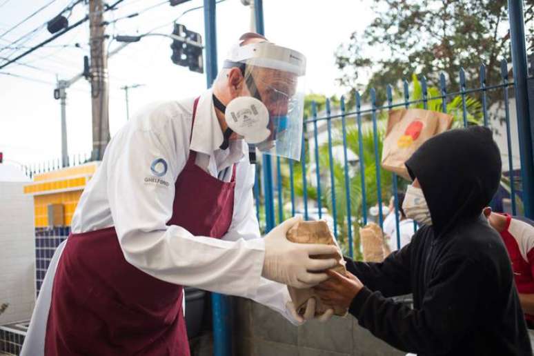 Padre Júlio Lancellotti entrega alimento a uma criança durante a pandemia de covid-19