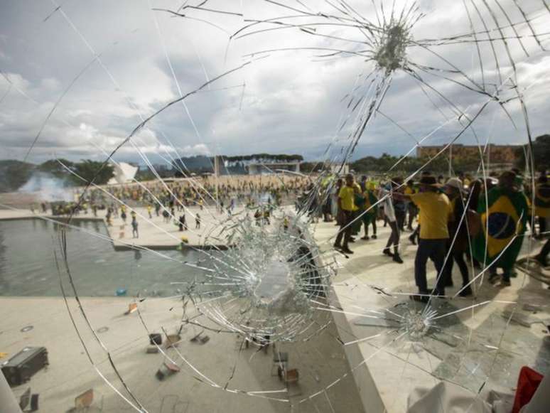 Imagem mostra vidraça quebrada e manifestantes bolsonaristas em Brasília.