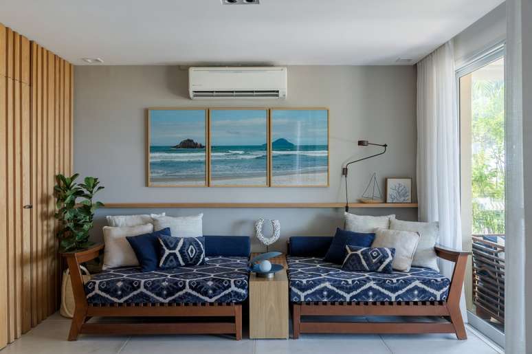 A vista da sala desta casa de praia &eacute; o mar de Juquehy. Projeto de Beatriz Quinelato. Na foto, sala com chaise azul, parede ripada e vista pra varanda.