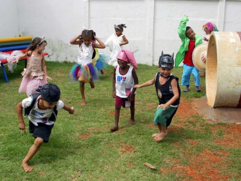 Imagem mostra crianças fantasiadas brincando juntas em um playground.