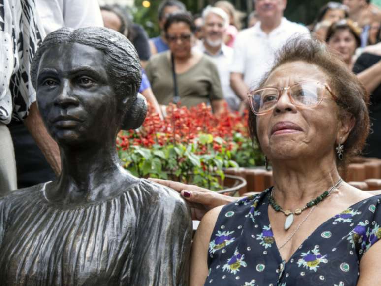 A imagem mostra a estátua de Enedina Alves ao lado de sua sobrinha, uma senhora negra. A foto foi tirada no dia da inauguração da escultura.