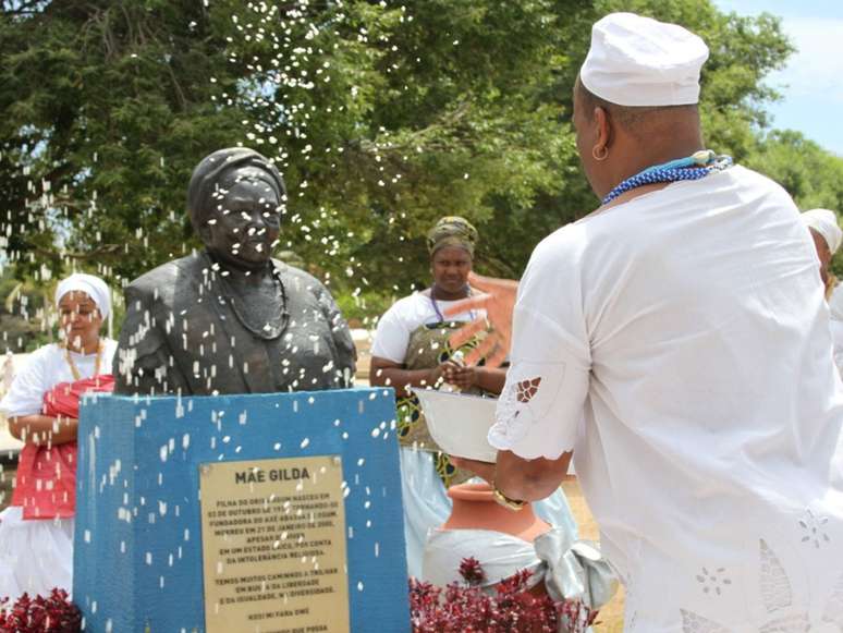 Imagem mostra um homem negro, de religião de matriz africana, reverenciando a estátua de Mãe Gilda.