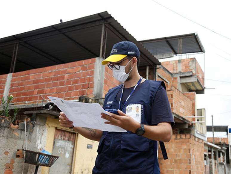 Imagem mostra recenseador, em primeiro plano, no teste para o Censo 2022 na comunidade Zumbi dos Palmares em Nova Iguaçu, Rio de Janeiro.