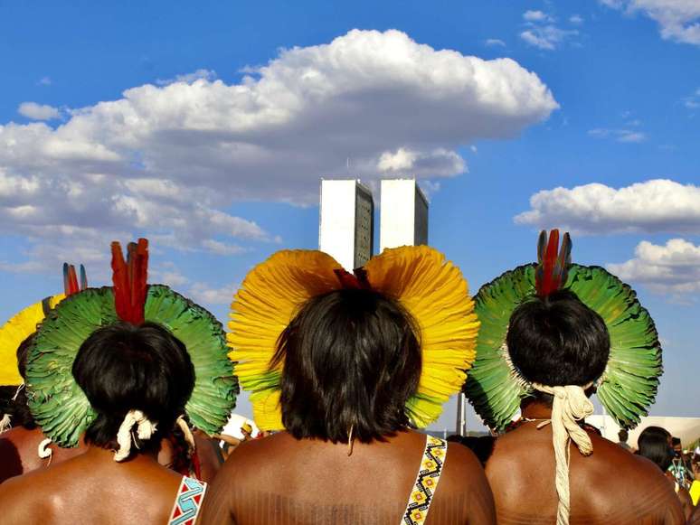 Imagem mostra três indígenas de costas para a câmera.