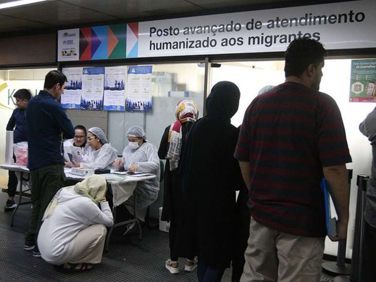 A imagem mostra um posto de atendimento humanizado para imigrantes e refugiados no Aeroporto de Guarulhos em São Paulo. Afegãos aguardam atendimento.