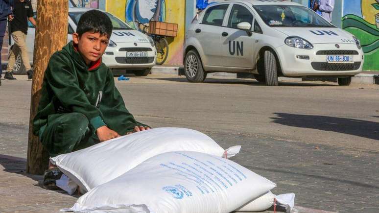 Criança ao lado de mantimentos dados pela agência da ONU em Gaza